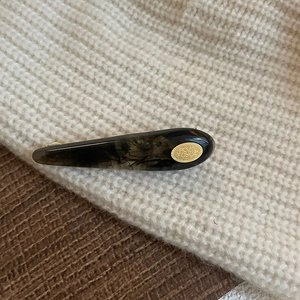 Amber tortoiseshell acetate hair clip with gold logo detail on a cozy knit beanie