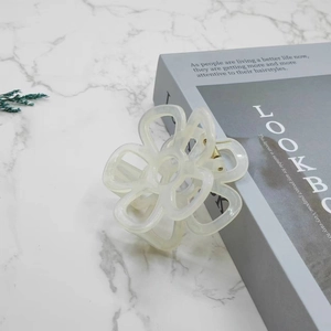 Detail view of a cream-white floral hair claw clip on a minimalist marble background