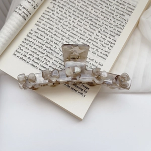 Grande molletta per capelli marmorizzata con cinque fiori di strass su un libro