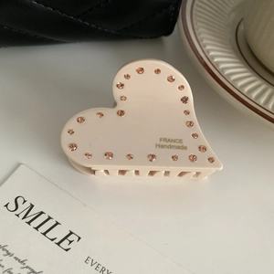 Dettaglio di un fermaglio per capelli a cuore beige in acetato con strass arancioni e testo