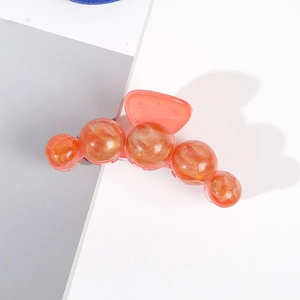 Gros plan sur une grande pince à cheveux orange avec perles marbrées pour un style élégant