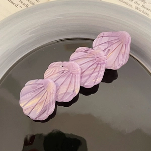 Détail d'une pince à cheveux violette en acétate en forme de coquillage sur un plat