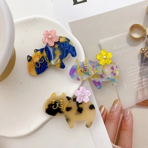 Detailed view of three cat-shaped acetate hair clips with floral patterns and gold outlines