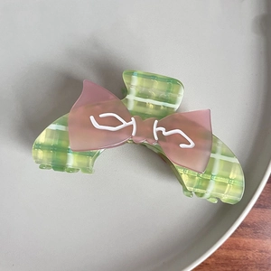 Pink and green plaid checkered hair claw clip with bow design on a minimalist tray