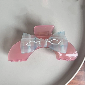 Pink jelly hair claw clip with a blue checkered bow on a minimalist ceramic plate