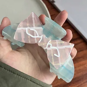 Pink and green plaid bow hair claw clip made of glossy acetate held by hand