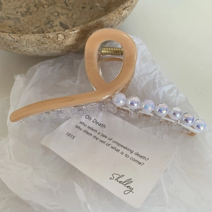 Détail d'une pince à cheveux abricot avec perles irisées et ressort en métal doré