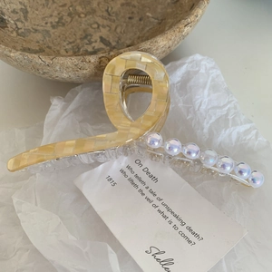 Détail d'une pince à cheveux à carreaux avec perles irisées sur papier texturé blanc