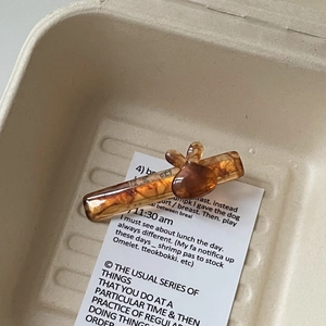 Détail d'une pince à cheveux lapin en acétate marron avec base ambre sur une carte beige