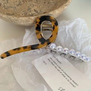 Détail d'une pince à cheveux en écaille avec perles irisées sur un bol en céramique