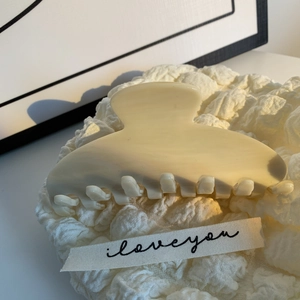 Détail d'une pince à cheveux en acétate blanc crème montrant la texture et les dents