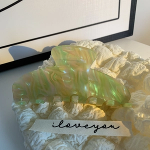 Gros plan d'une pince à cheveux en acétate irisé vert et rose sur tissu blanc texturé