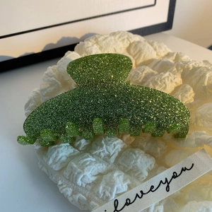 Détail d'une pince à cheveux vert pailleté avec reflets argentés sur tissu blanc