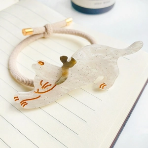 Gros plan d'un chouchou chat en acétate avec embouts dorés et cordon élastique crème