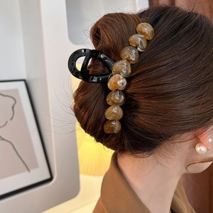 Large black hair claw clip with amber heart patterns on an elegant updo hairstyle