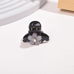 Detailed macro view of a black floral hair claw clip with grey-blue matte flower and zircon