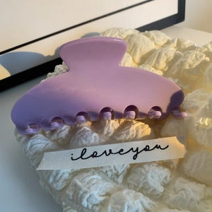 Détail d'une pince à cheveux en acétate violette sur un tissu blanc doux texturé