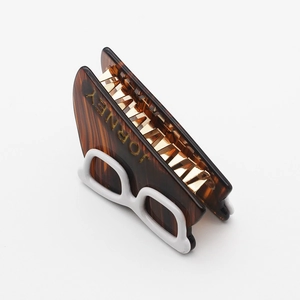 Close-up of tortoise shell acetate hair claw with white glasses detail and gold lettering