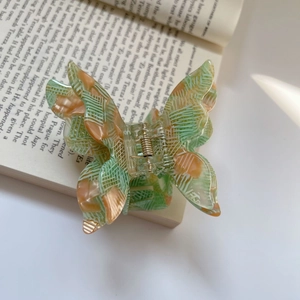 Detail of green and orange acetate butterfly hair claw clip with golden metal spring
