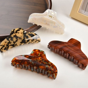 Detail of four acetate hair claws in pearl, tortoiseshell, and wood patterns with gold logo