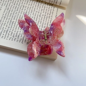 Detail of pink and purple acetate butterfly hair claw with gold spring on a book