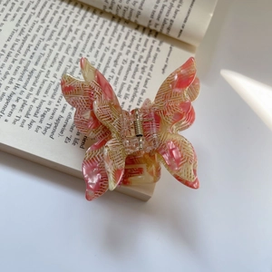 Detail of pink acetate butterfly hair claw with woven texture pattern on a book