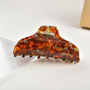 Detailed close-up of tortoise shell pattern acetate hair claw clip on white surface