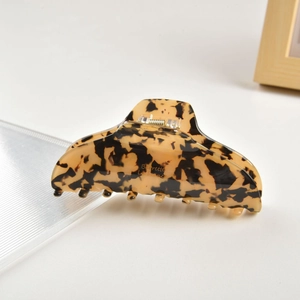 Detail view of tortoiseshell acetate hair claw clip with golden lettering on a white tray