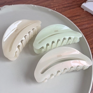 Three large vintage acetate hair claws in beige, green, and pearl white on a plate