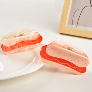 Detailed view of creative hot dog shaped acetate hair claws in cream and pink on a white plate