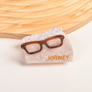 Détail de la pince à cheveux en acétate forme lunettes avec gravure dorée JORNEY sur le côté