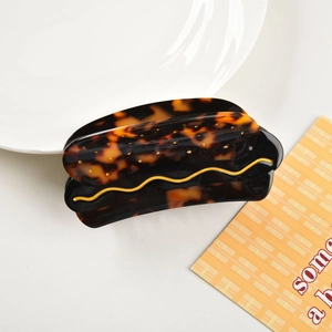 Macro detail of tortoiseshell acetate claw clip with a wavy gold metallic line accent