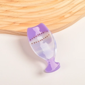 Détail de la pince à cheveux en acétate violette ornée de strass roses sur fond blanc
