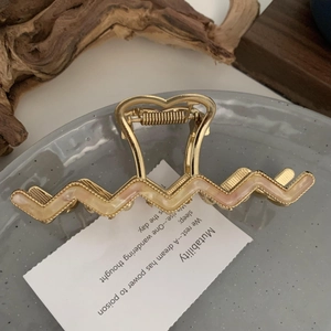 Detail of wavy acetate hair claw with gold heart handle and pink enamel inlay