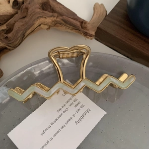 Close-up of golden wavy hair claw clip with mint green inlay and heart-shaped handle