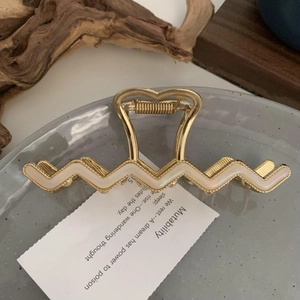 Detail of golden wavy metal hair claw clip with ivory inlay on a poetic display tray