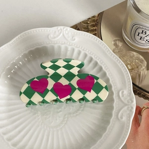 Close-up of green and white checkered heart hair claw clip on decorative ceramic plate