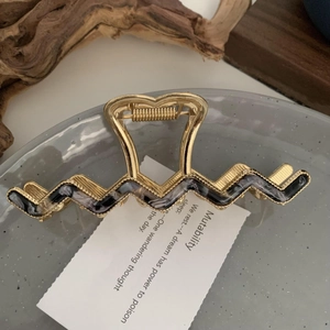 Detailed view of wave-shaped gold metal hair claw clip with marble texture on grey plate