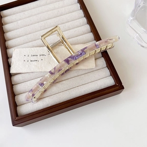 Macro detail of purple marble acetate inlay on gold metal claw clip on a jewelry tray