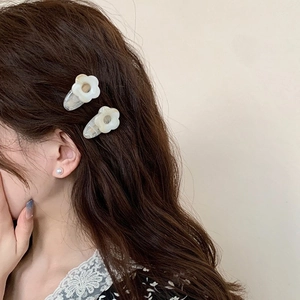 Vue détaillée de deux barrettes fleurs crème portées sur des cheveux bruns ondulés