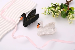 Detailed view of swan-shaped hair clips in black and pearl white with gold accents