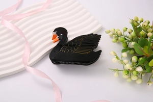 Detailed close-up of black swan hair claw clip with golden patterns and acetate finish