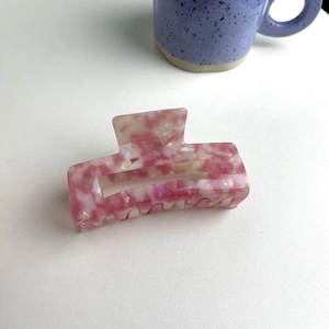 Detailed top view of a large pink marble acetate hair claw clip on white table
