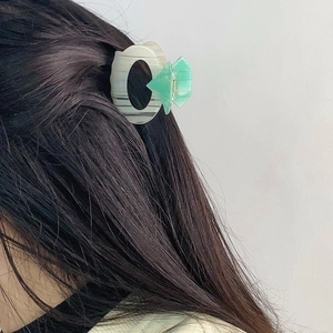 Elegant geometric star hair claw clip in beige and mint green on dark wavy hair