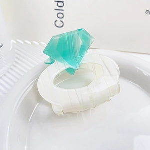 Detail view of a diamond-ring-shaped green and white shark hair clip with vertical texture