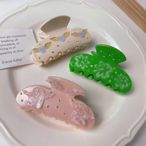 Close-up of three acetate hair claws with heart and floral designs in a ceramic dish