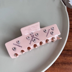 Detail of pink resin hair claw clip with heart-shaped rhinestones on a wooden surface