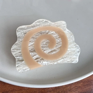 Detail of a spiral cream acetate hair claw clip with icy textures on wood surface
