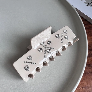 Detailed view of beige acetate hair claw with rhinestones in K pattern on ceramic plate