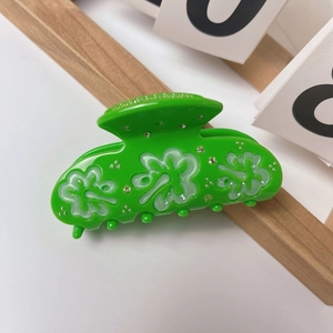 Close-up of green acetate hair claw clip featuring white clover patterns and small rhinestones